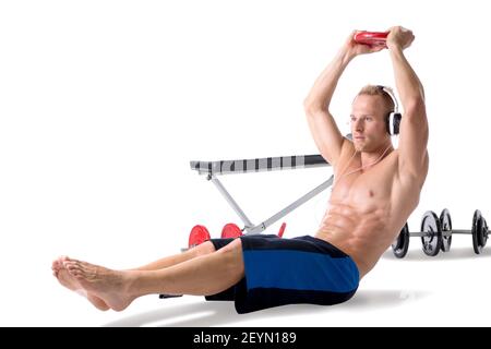 Un jeune homme blond musclé qui soulève des poids et écoute de la musique dans un casque Banque D'Images