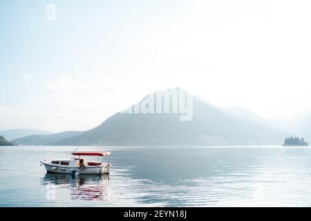 Bateau à moteur blanc de plaisir avec un soleil rouge qui s'épare contre la toile de fond des montagnes dans le brouillard. Banque D'Images