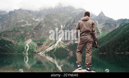 Un homme grimpe une pierre près de la rive d'un lac de montagne pittoresque avec de l'eau émeraude. Vue magnifique sur la nature. Concept de voyage et de mode de vie sain. Banque D'Images
