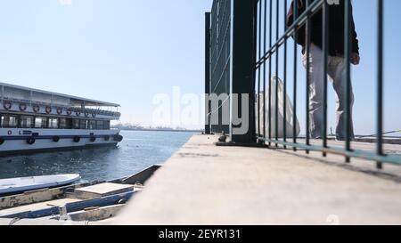 istanbul. Turquie. Bosphore istanbul. Homme derrière les clôtures en métal vert qui vend du caffe et du thé sur la rive de Kadikoy avec ferry sur le port. Banque D'Images