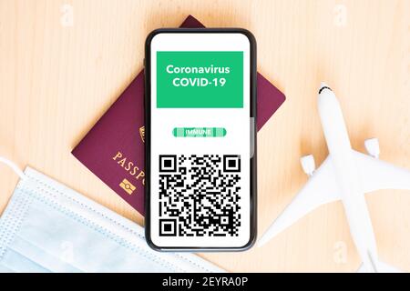 Un masque facial, un modèle d'avion, un passeport et un smartphone avec un coronavirus, carte d'immunité COVID-19 sont disposés sur un bureau. Banque D'Images