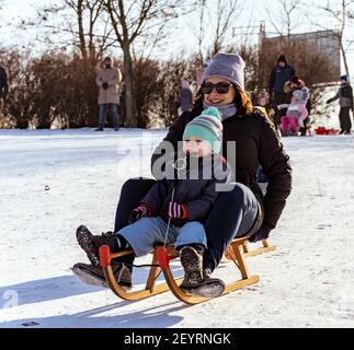 POZNAN, POLOGNE - 17 janvier 2021 : une femme souriante et un petit garçon caucasien polonais de trois ans, assis sur un toboggan en bois sur une colline enneigée dans un parc Banque D'Images