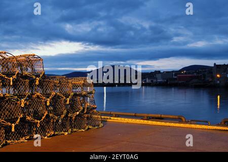 Cages de crabe et de homard dans le port écossais avec bleu nuages maisons éloignées et grande colline en arrière-plan Banque D'Images