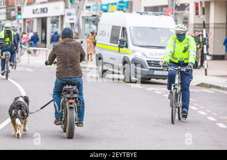 Cork, Cork, Irlande. 06e mars 2021. Un homme emmène son chien pour une promenade tandis qu'un Garda regarde pendant une manifestation dans les rues de Cork City pour protester contre le maintien du gouvernement. Un plan de police, qui comprenait des unités d'ordre public, était en place pour l'événement qui a eu lieu sur Patrick Street dans l'après-midi Gardai ont également averti que des poursuites pénales ou des amendes pourraient survenir pour ceux qui bafouent les restrictions actuelles de niveau 5 Covid-19.- crédit; David Creedon / Alamy Live News Banque D'Images