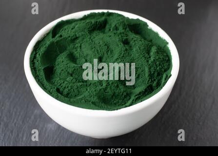 Poudre de spiruline dans un bol blanc sur fond noir. Concept d'alimentation saine. Orientation horizontale. Gros plan. Banque D'Images