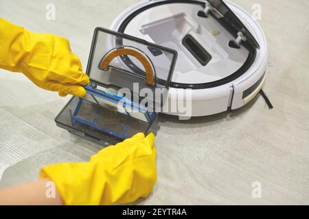 Boîte de rangement à poussière boîte d'aspirateur robotique à mains féminines gantées. Femme dans des gants de protection en sortant le récipient et le filtre pour le nettoyer de di Banque D'Images