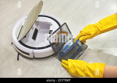 Boîte de rangement à poussière boîte d'aspirateur robotique à mains féminines gantées. Femme dans des gants de protection en sortant le récipient et le filtre pour le nettoyer de di Banque D'Images