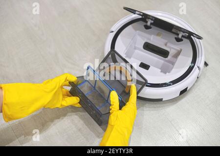 Boîte de rangement à poussière boîte d'aspirateur robotique à mains féminines gantées. Femme dans des gants de protection en sortant le récipient et le filtre pour le nettoyer de di Banque D'Images