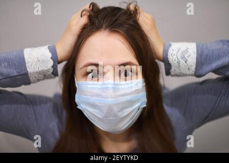 Gros plan portrait d'une femme effrayée dans un masque médical de protection, saisissant sa tête. Concept de la peur et de la panique de la maladie respiratoire, coronavirus, Banque D'Images