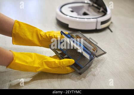 Boîte de rangement à poussière boîte d'aspirateur robotique à mains féminines gantées. Femme dans des gants de protection en sortant le récipient et le filtre pour le nettoyer de di Banque D'Images