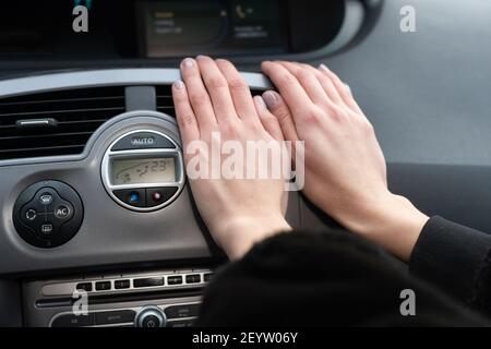 Une femme garde ses mains au froid sur un chauffe-voiture. Il réchauffe vos mains avec de l'air chaud. Banque D'Images