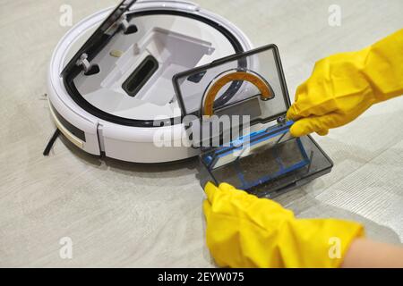 Boîte de rangement à poussière boîte d'aspirateur robotique à mains féminines gantées. Femme dans des gants de protection en sortant le récipient et le filtre pour le nettoyer de di Banque D'Images