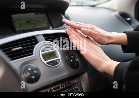 Une femme garde ses mains au froid sur un chauffe-voiture. Il réchauffe vos mains avec de l'air chaud. Banque D'Images