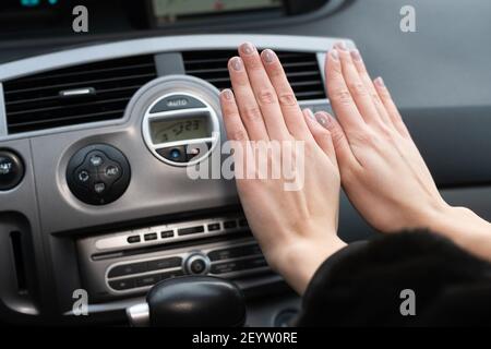 Une femme garde ses mains au froid sur un chauffe-voiture. Il réchauffe vos mains avec de l'air chaud. Banque D'Images