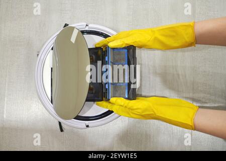 Boîte de rangement à poussière boîte d'aspirateur robotique à mains féminines gantées. Femme dans des gants de protection en sortant le récipient et le filtre pour le nettoyer de di Banque D'Images