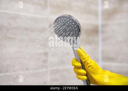 Femme main dans un gant de protection en caoutchouc tenant la pomme de douche avec l'eau dans la salle de bains, l'espace de copie, le flou de mouvement. Banque D'Images