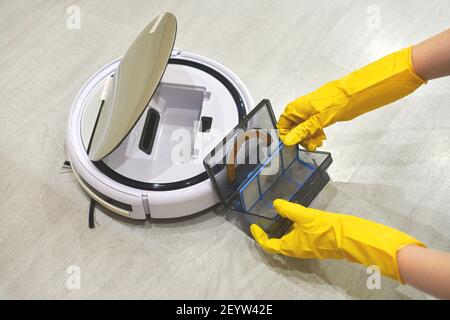 Boîte de rangement à poussière boîte d'aspirateur robotique à mains féminines gantées. Femme dans des gants de protection en sortant le récipient et le filtre pour le nettoyer de di Banque D'Images
