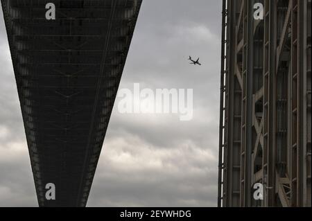 Avion vu contre un ciel nuageux à travers la structure métallique du pont George Washington. Banque D'Images