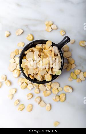 Petits haricots secs non décortiqués dans une tasse noire sur du marbre blanc. Fava bean. Banque D'Images