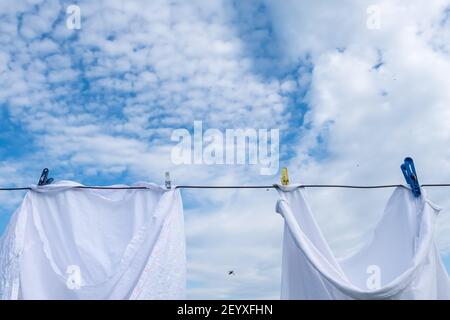 La literie propre et lavée est séchée sur une corde avec des épingles à linge à l'air libre, sur un fond de ciel bleu et de nuages. Banque D'Images