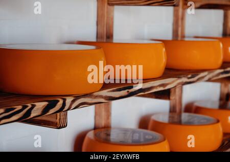 Roue de fromage de chèvre sur le rack dans l'entrepôt de l'usine. Plusieurs têtes de fromage mûres sont exposées sur les étagères de la boutique de fabrication de cheesmaking Banque D'Images