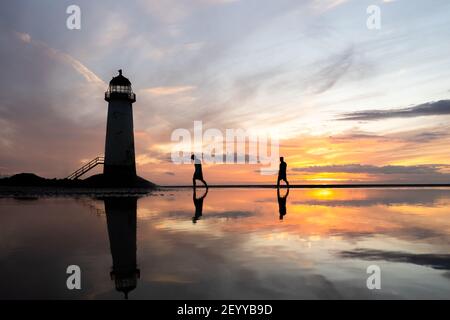 Beau phare au bord de la mer Golden hour coucher de soleil avec reflet de les gens qui marchent à travers les piscines d'eau de mer de marée arrive dans la réflexion du soleil à l'horizon Banque D'Images