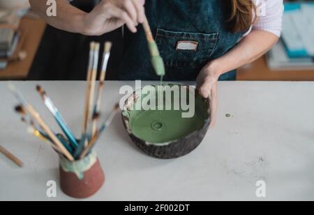 Femme mélangeant la peinture avec la brosse à l'intérieur de la cuvette en céramique dans l'atelier studio - concept artisanal artistique et créatif Banque D'Images
