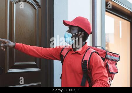 Un cavalier africain qui fournit un repas à ses clients à domicile tout en les portant Masque facial pendant l'épidémie de virus corona - concept de la livraison de nourriture Banque D'Images