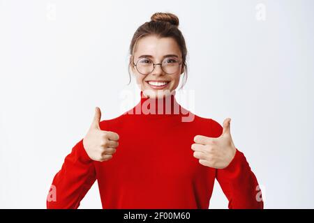 Portrait d'une femme d'affaires en lunettes de bonne apparence louent excellent travail, montrant les pouces jusqu'à approuver et comme quelque chose, donnant des commentaires positifs et Banque D'Images