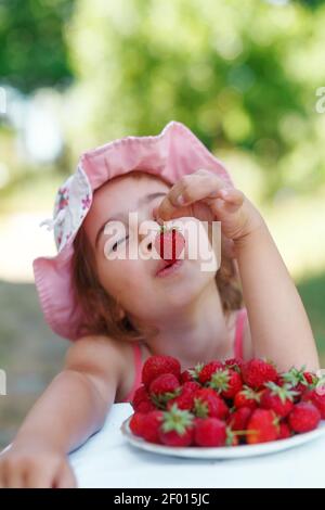 Portrait de la jeune fille heureuse et mignonne mange des fraises le jour de l'été. Mise au point douce Banque D'Images