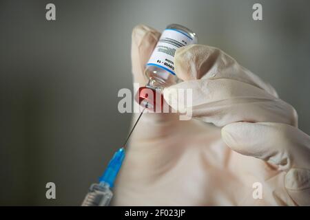 Mains gantées d'un médecin ou d'une infirmière tenant une seringue et petite flacon avec vaccin tout en préparant l'injection pour le patient avec covid19 dans les cliniques Banque D'Images