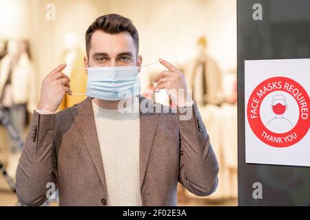 Portrait d'un jeune homme regardant l'appareil photo et mettant sur le masque à l'intérieur Banque D'Images