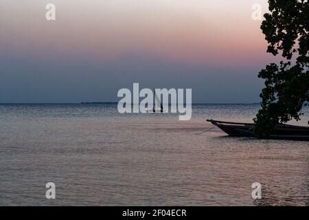 Côte de l'île de Zanzibar (Tanzanie, archipel de Zanzibar). Bateaux aborigènes typiques dans la région à l'avant-plan et au crépuscule. Océan avec le voilier. Banque D'Images