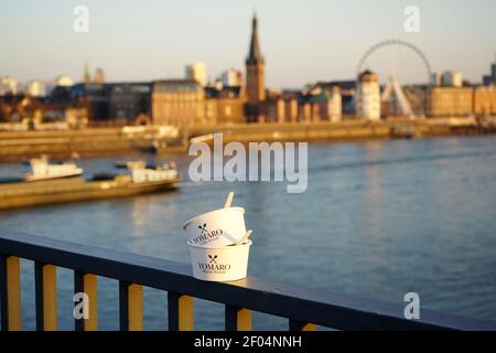 Deux tasses en papier yaourt glacé « Yomaro » sur la balustrade du pont Oberkasseler au bord du Rhin avec la vieille ville historique dans un fond flou. Banque D'Images