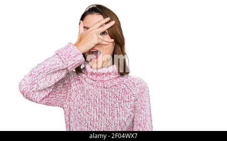 Jeune fille caucasienne portant la laine hiver chandail peeking en choc couvrant le visage et les yeux avec la main, regardant à travers les doigts avec l'expressio embarrassée Banque D'Images