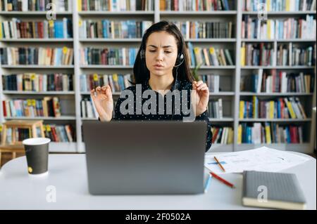 Une femme ciblée qui travaille comme opérateur d'un centre d'appels, communique avec les clients. Une femme d'affaires caucasienne dans un micro-casque/une oreillette s'assoit au bureau, parle par appel vidéo avec ses collègues du plan d'affaires Banque D'Images