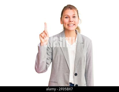 Jeune belle femme blonde portant une veste élégante montrant et pointant vers le haut avec le doigt numéro un tout en souriant confiant et heureux. Banque D'Images