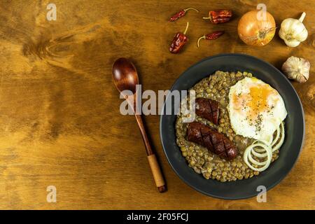 Lentilles avec saucisse et piment. Saucisse grillée et lentilles avec œuf sur une assiette noire. Légumineuses. Une alimentation saine. Banque D'Images