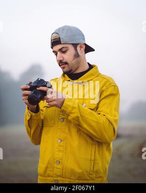 Jeune photographe masculin en veste denim jaune prenant des photos appareil photo sur un arrière-plan flou et brumeux Banque D'Images