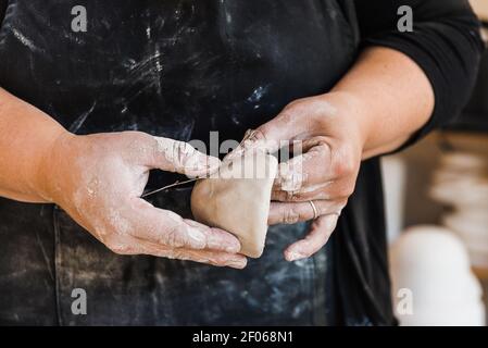 Crop anonyme maître dans le tablier sale debout dans l'atelier et morceau de façonnage d'argile le marquant avec la fleur dans les mains Banque D'Images