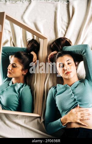 Vue de dessus de la femme millénaire avec la main derrière la tête à l'appareil photo contre le miroir sur un tissu froissé Banque D'Images