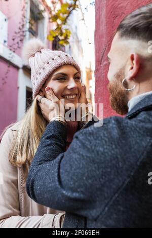 Vue latérale d'une récolte tendre homme méconnaissable embrassant une charmante femme souriante tout en se tenant debout en ville pendant la promenade Banque D'Images