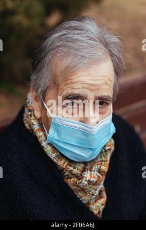Portrait d'une femme âgée avec masque facial regardant l'appareil photo tout en étant assise sur un banc de parc Banque D'Images