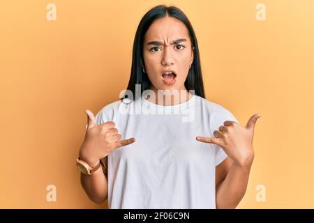 Jeune femme asiatique faisant le signe de shaka avec les mains dans le visage de choc, regardant sceptique et sarcastique, surpris par la bouche ouverte Banque D'Images