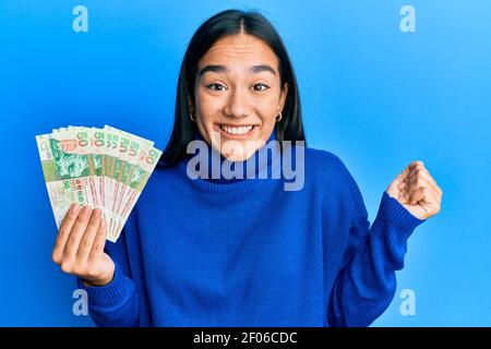 Une jeune femme asiatique qui détient 50 billets de banque en dollars de hong kong criait fière, célébrant la victoire et le succès très excitée par le bras relevé Banque D'Images