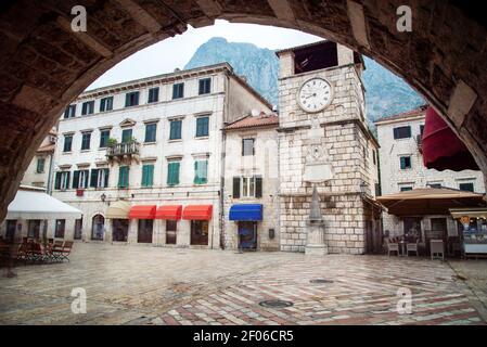 Vue sur la place principale et la vieille tour de l'horloge depuis le dessous de l'arcade de la porte de la mer menant à la vieille ville de Kotor. Banque D'Images