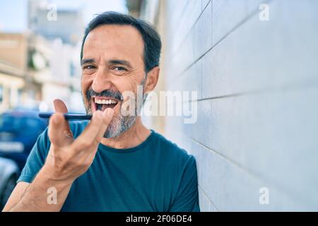 Homme d'âge moyen avec barbe souriante plein air envoi de la voix message sur le téléphone Banque D'Images