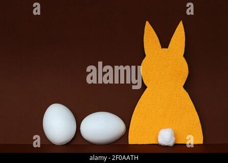 Arrière-plan de Pâques. Un lapin jaune en feutre avec deux œufs sur fond de papier brun Banque D'Images