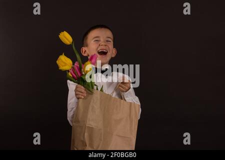 le garçon avec le vitiligo dans une chemise blanche et un Noeud papillon avec tulipes sur fond noir Studio Banque D'Images