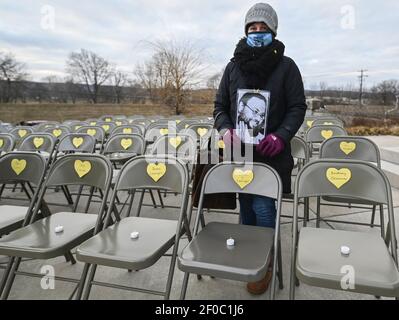 Wilkes barre, États-Unis. 06e mars 2021. Une femme tenant une photo d'une victime Covid 19, se tient entre les rangées de chaises vides avec des symboles de coeur et des bougies allumées, pendant l'événement. Un mémorial et une vigile pour les victimes de Covid19 ont eu lieu à l'extérieur du palais de justice du comté de Luzerne dans le cadre du projet du Mémorial du cœur jaune. Une chaise vide a été placée pour représenter chacune des vies perdues dans la collectivité. Crédit : SOPA Images Limited/Alamy Live News Banque D'Images